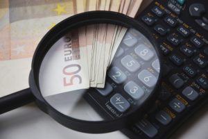 A magnifying glass on top of a calculator and a lot of 50 euro bills